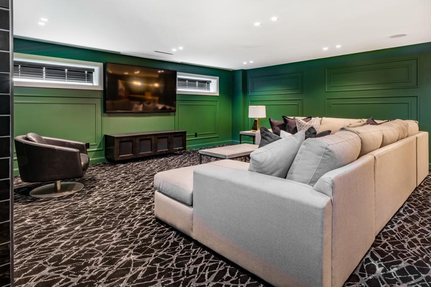 Basement living room with unique flooring, couches, green wall lamp, and ceiling lights