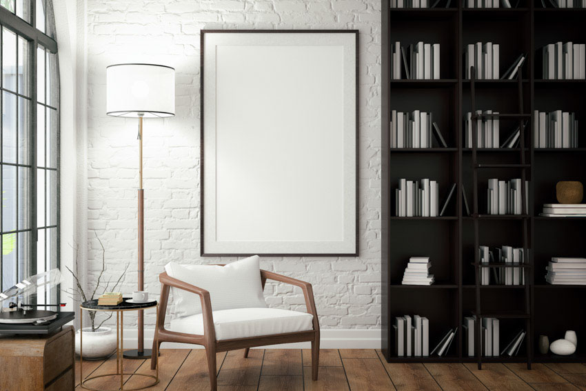 Basement living space with bookshelf, wood floor, chair, windows, white wall, and tall floor lamp