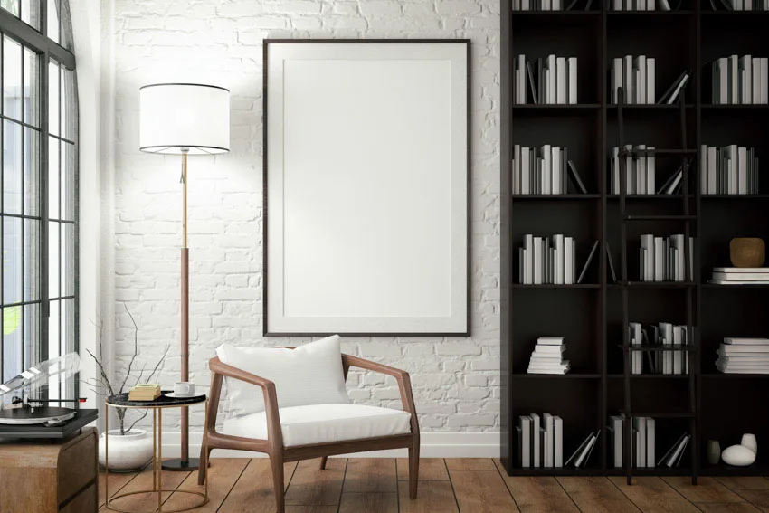 Room with bookshelf, wood floor, chair, windows, white wall, and tall floor lamp
