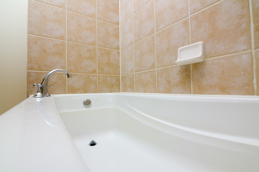 Bathroom area with tile wall, acrylic tub, faucet, and drain