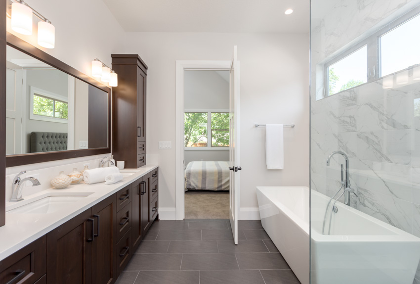 Bathroom with acrylic tub, tile floor, white countertop, mirror cabinets, windows, and accent lighting