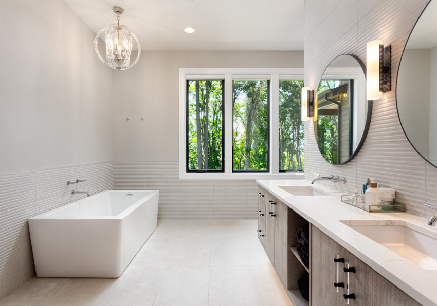 Bathroom with acrylic tub, white wall, countertop, mirror, cabinets, and windows