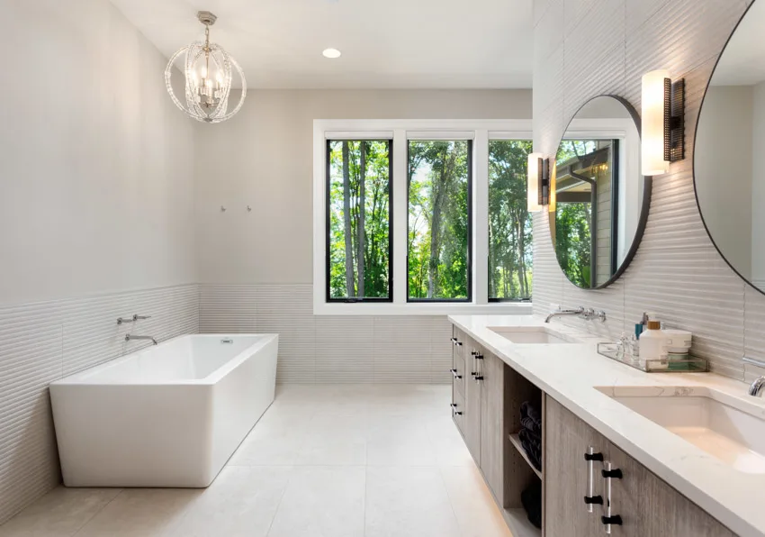 Bathroom with half tile white wall, countertop, mirror, cabinets, and windows