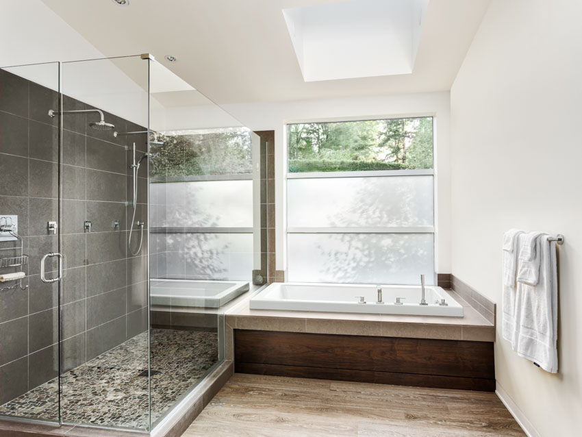 Bathroom with fiberglass tub, shower area, glass door, windows, wood floor, and skylight