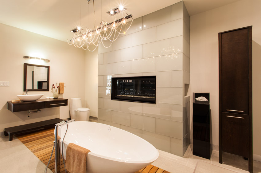 Bathroom with tub and fireplace, hanging light, and mirror