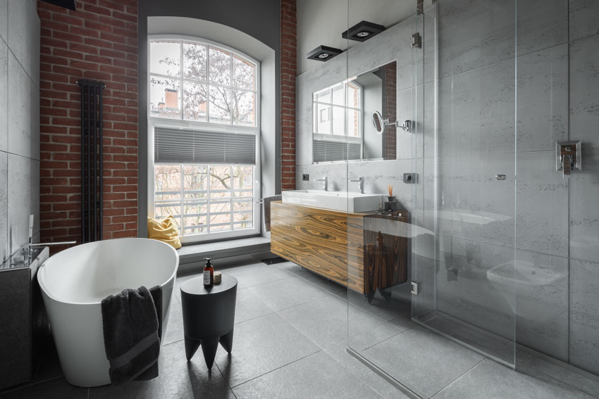 Bathroom with slate flooring, tub, sink, mirror, brick accent wall, and window