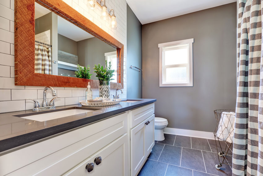 Bathroom with slate tile floor, window, countertop, cabinets, backsplash, and mirror