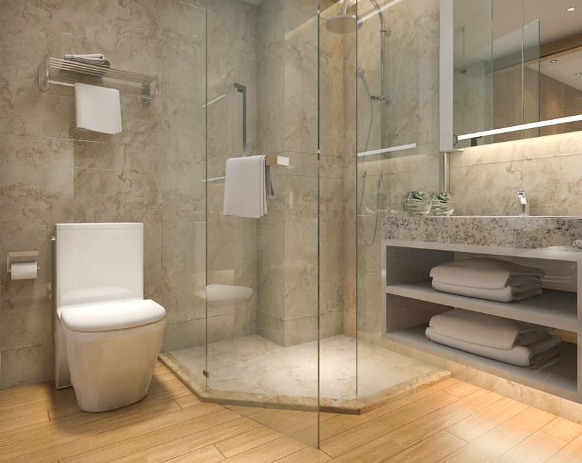 Bathroom with stone resin shower wall and floor, toilet, mirror, and glass divider