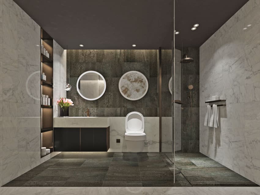 Bathroom with stone resin walls, shower area, slate tile floor, mirrors, toilet, and sinks