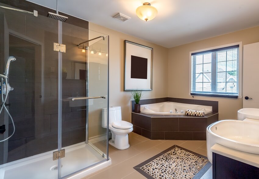 Beige warm bathroom with accent stone tile floor, walk-in shower, corner bathtub, and double sink