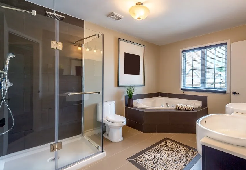 Beige warm bathroom with accent stone floor, walk-in shower, corner bathtub, and double sink