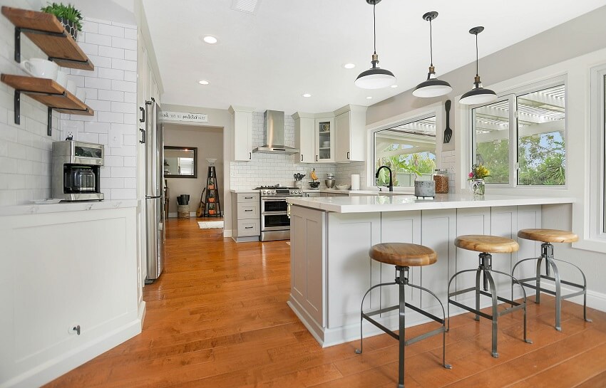 Bright kitchen with brown wood floor, floating shelves, and pendant lights above island with stools