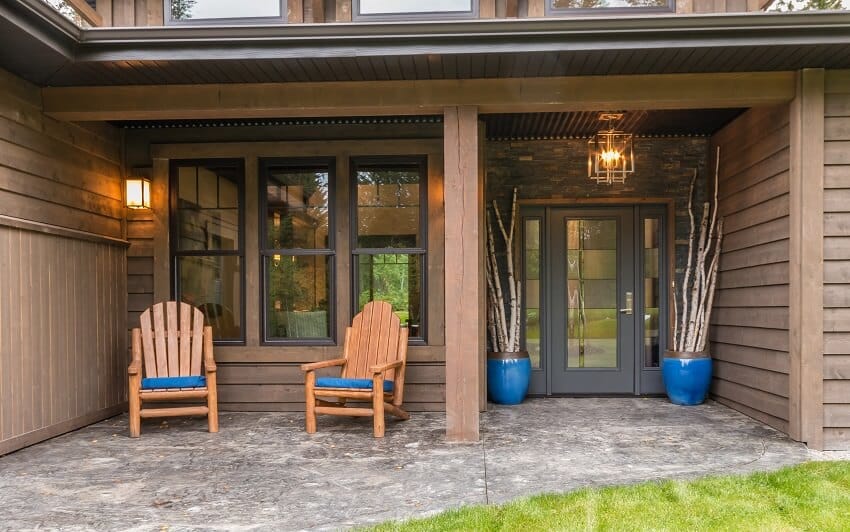 Brown front porch with lighting fixtures, blue pots, and wood chairs with blue cushion