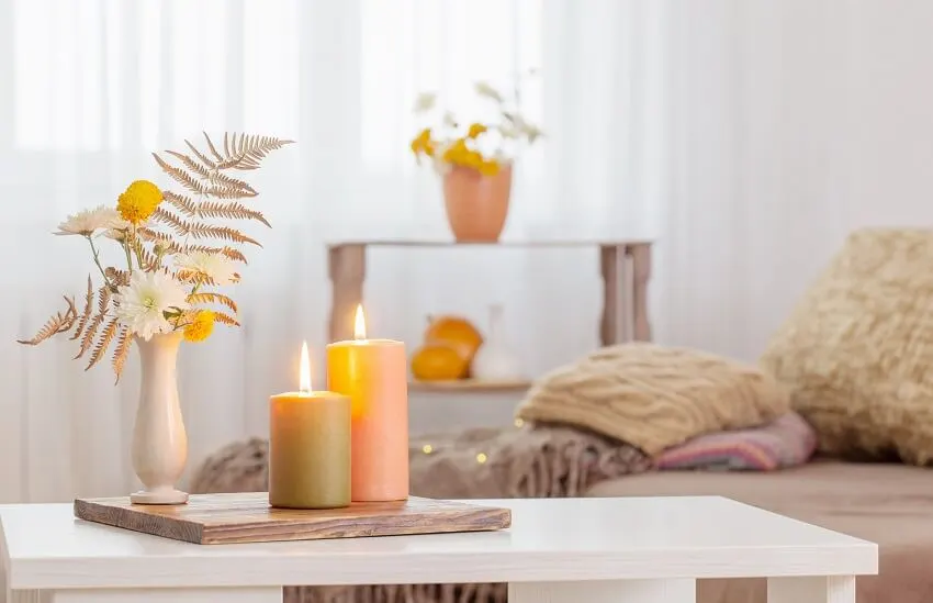 Burning candles with autumn decor on white table and a sofa bed on the background