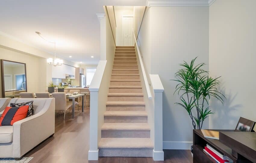 Carpeted stairs in a new house with wood floors, white walls, and furnishings