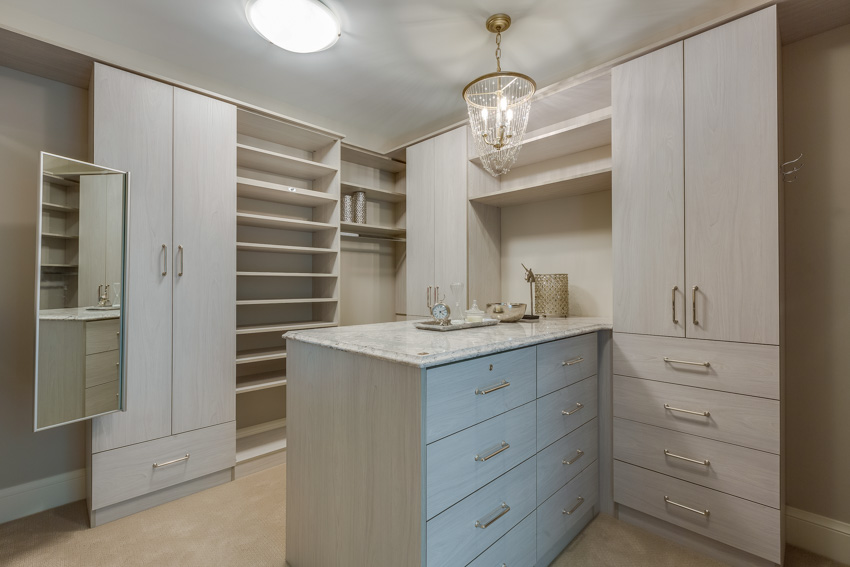 Closet with white cabinet doors, center island, drawers, and hanging lights