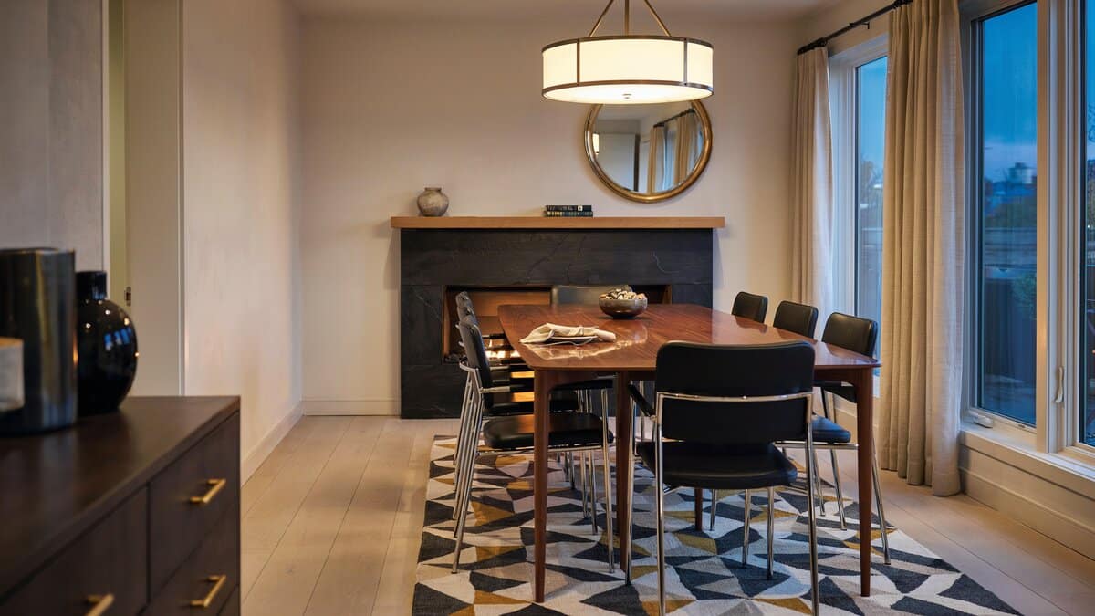 Modern dining table with black chairs, round pendant light, geometric floor, mounted mirror