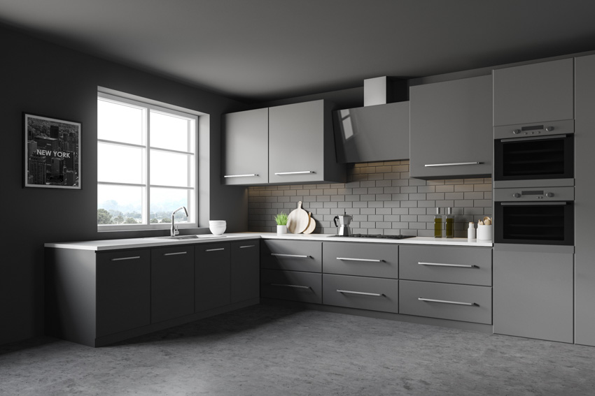 Dark themed kitchen with black cabinets, windows, tile backsplash, and gray flooring