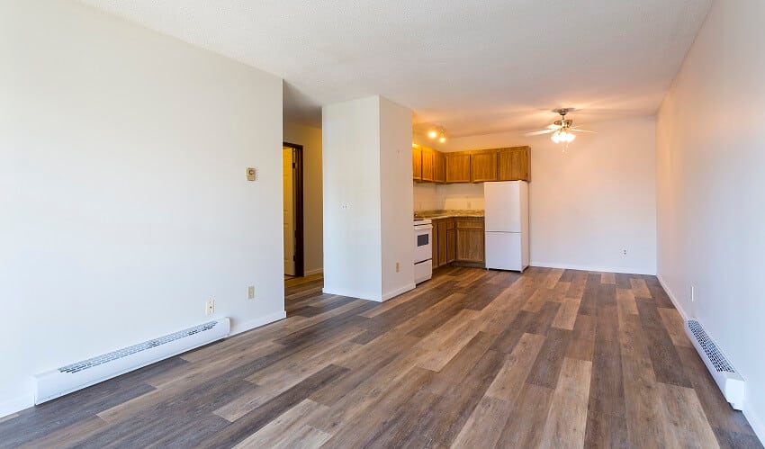 Empty apartment with laminate floors and electric baseboard heater on white walls