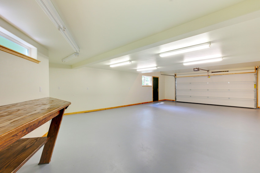 Empty garage with sealed floor, door, ceiling light, and wood bench