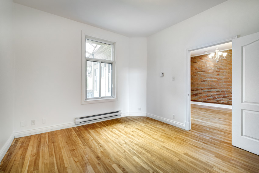 Empty room with wooden flooring, electric baseboard heater, windows, and white wall