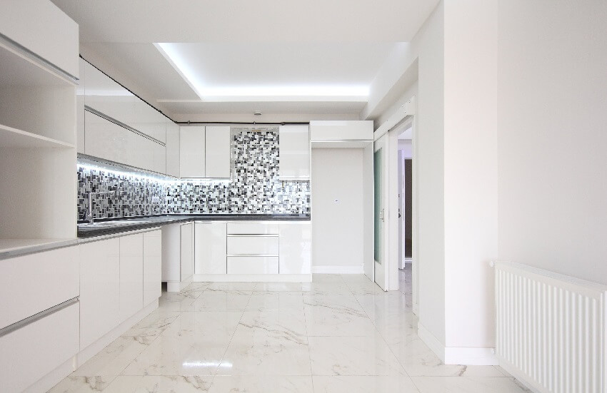 Empty white kitchen with marble tile floor, black countertops, and mosaic tile backsplash