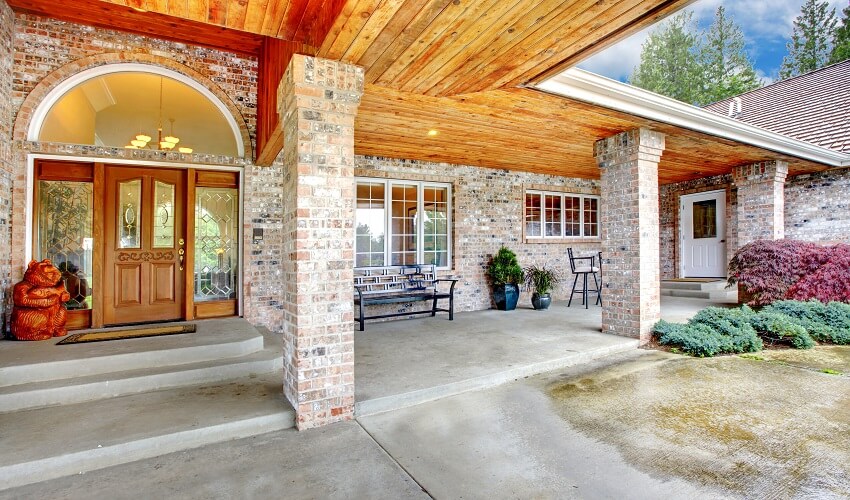 Entrance of a brick house with stained glass wooden door, brick columns, and front patio with concrete floor
