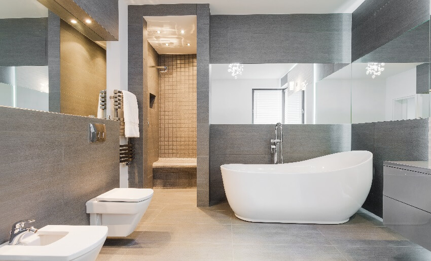 Freestanding bathtub in gray bathroom with wraparound wall mirrors