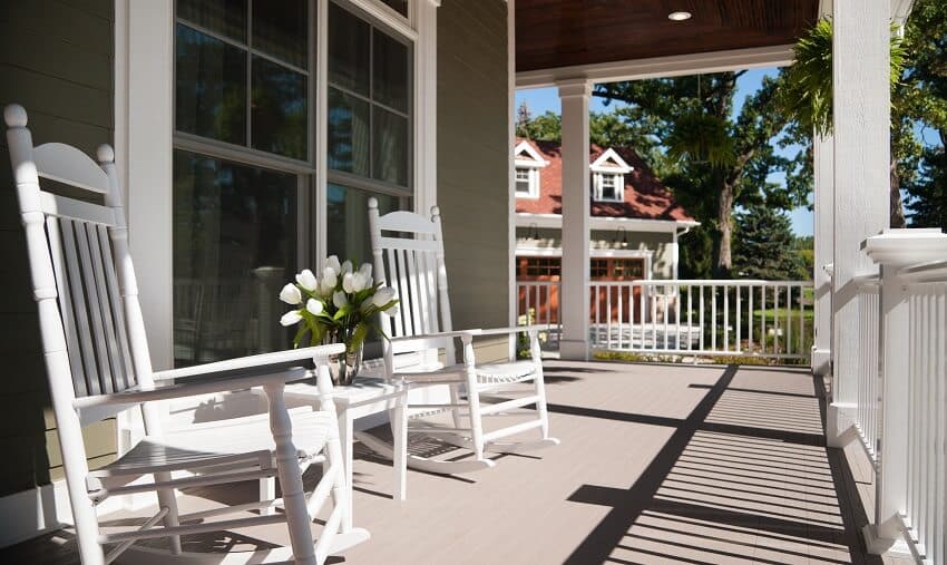 Front of the wrap around porch with two white rocking chairs and a vase of tulips
