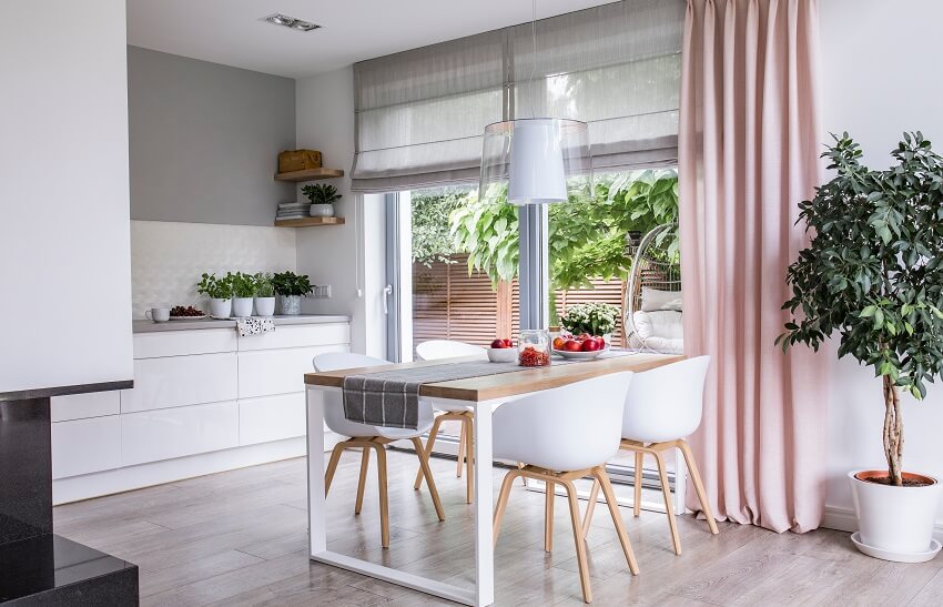 Gray roman shades and a pink curtain on big windows in a modern kitchen and dining room interior