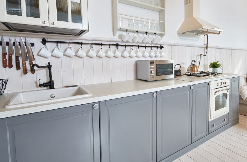 Grey and white kitchen with beadboard backsplash, range hood, and black kitchen rod with cups