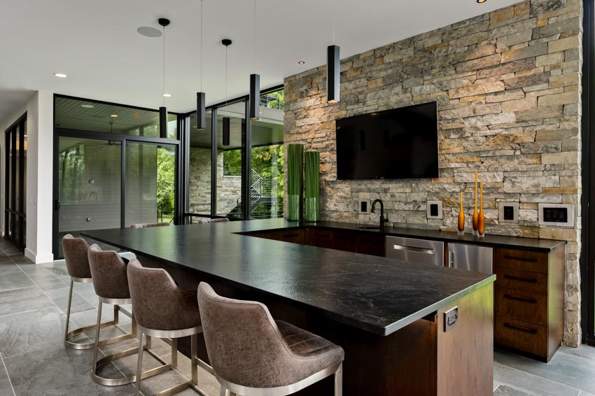 Home bar kitchen with stone accent wall, countertop, high chairs, and television