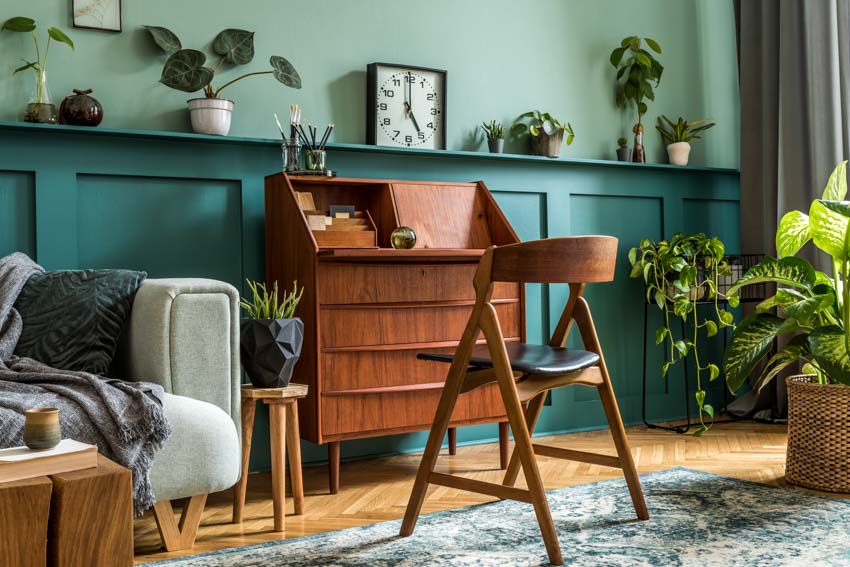 Home office with secretary desk, wood chair, couch, wooden flooring, and indoor plants