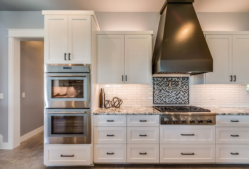 Huge range hood, accent backsplash behind stove, and white cabinets in a kitchen
