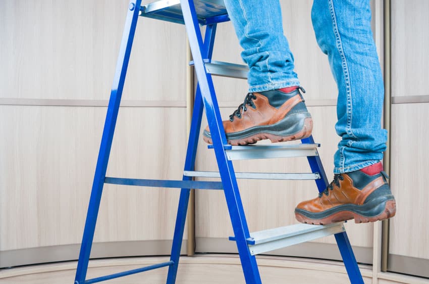 Individual climbing up a blue ladder