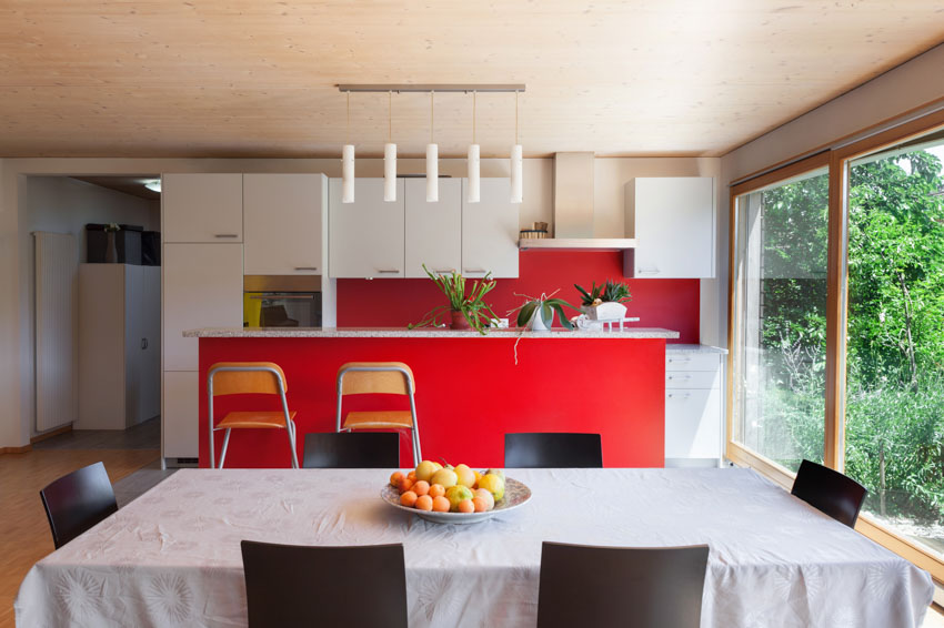 Kitchen and dining room combined red accent wall, hanging lights, white cabinets, and windows