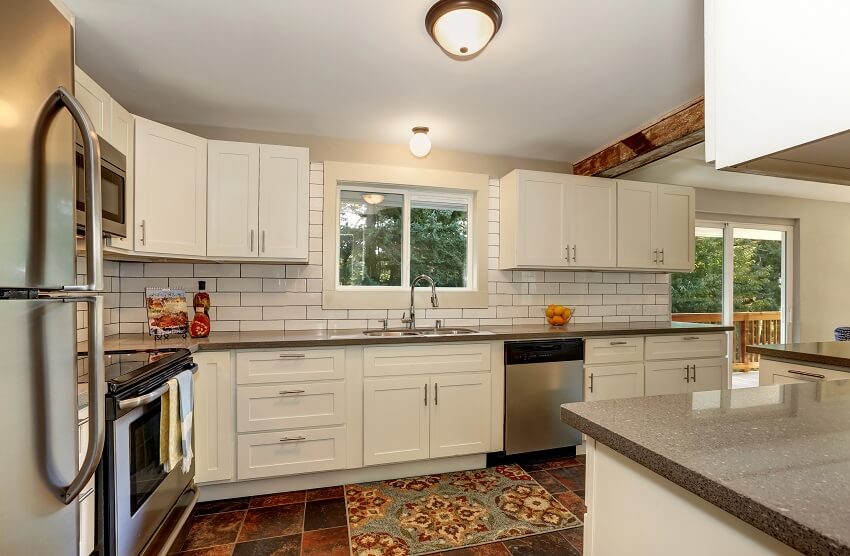 Kitchen interior with white cabinets, granite countertops, subway tile backsplash on open wall, and stone tile flooring