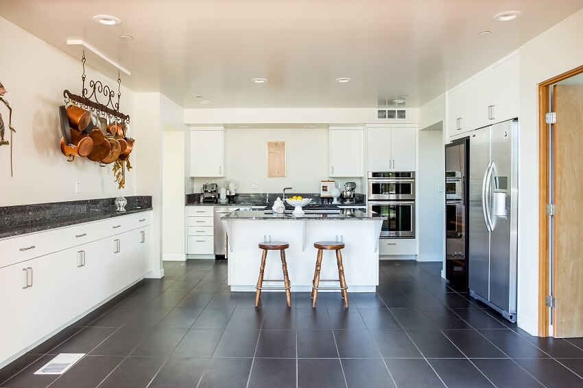 White kitchen cabinets with dark tile flooring and countertops