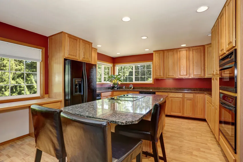 Kitchen with center table, agate countertop, red backsplash, wood cabinet, recessed lights, and windows