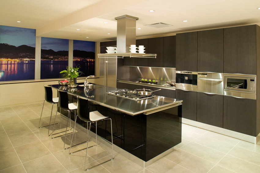 Kitchen with dark cabinets, metal countertop, tile flooring, center island, range hood, and windows