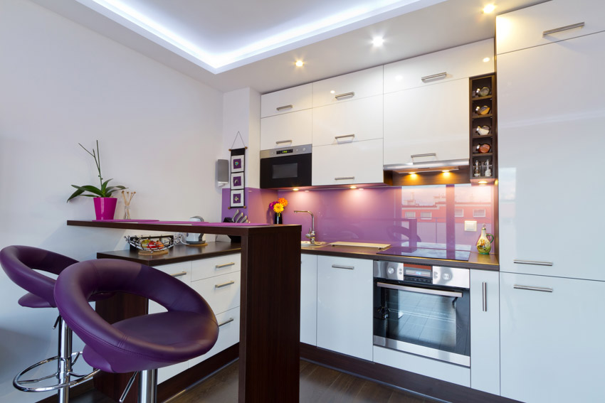 Kitchen with purple glass backsplash, high chair, white cabinets, and recessed lights