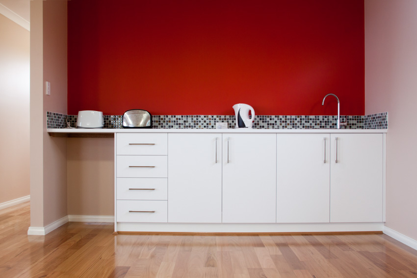 Kitchen with red accent wall, white cabinets, and wood floor