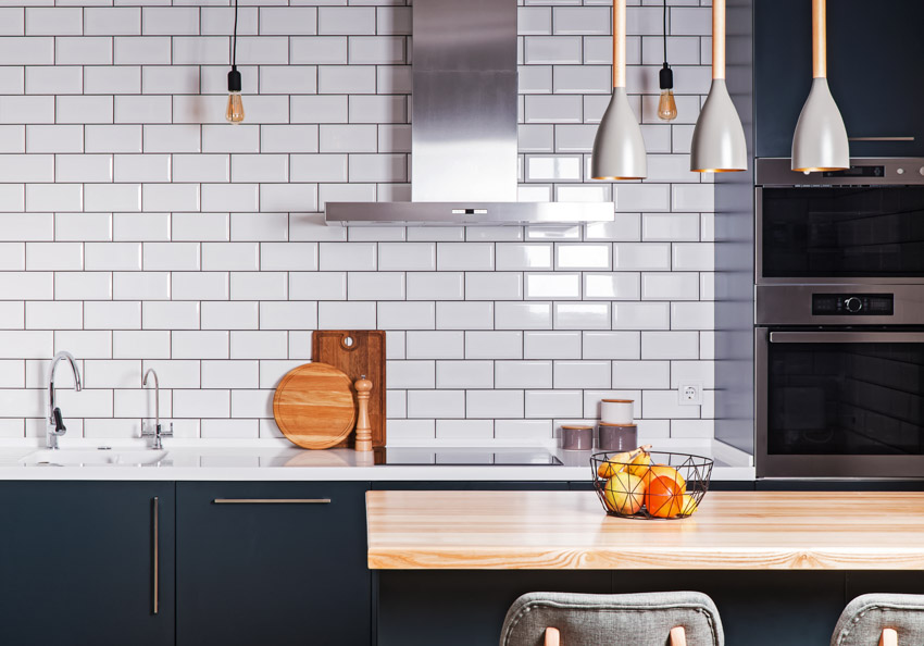 Kitchen with white subway tile accent wall, cabinets, range hood, and pendant lights