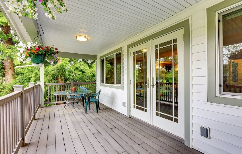 Large covered porch with railings, outdoor seats, flower pots, and french doors