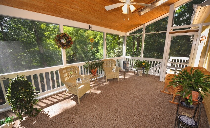 Large enclosed porch with ceiling panels and rocking chairs