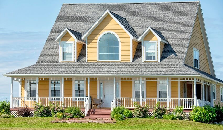 Large yellow country home with farmers porch, asphalt shingle roofing, and dormer windows