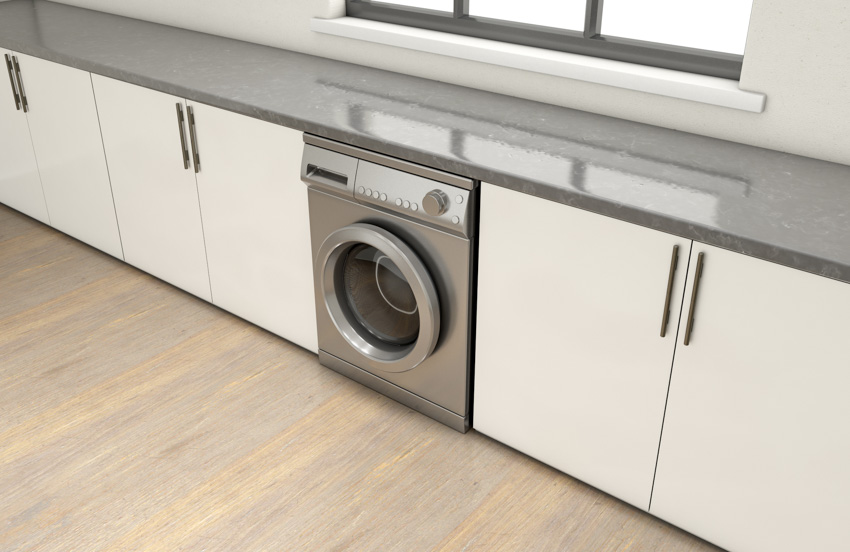 Laundry machine placed under countertop in a kitchen with white cabinets
