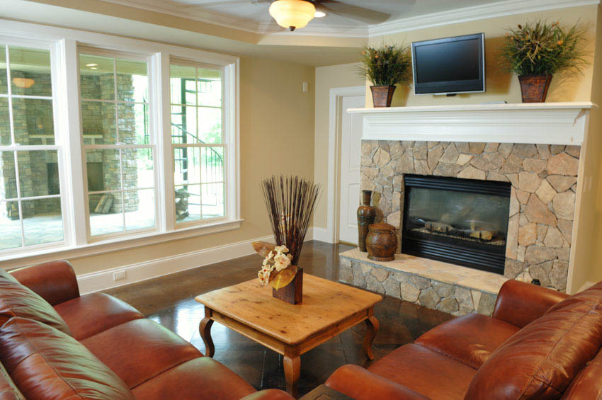 Living room with stone fireplace, mantel, indoor potted plants, leather couch, and windows