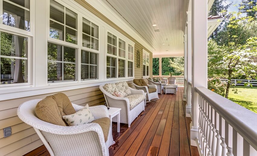Long porch with panel wood floor, white armchairs, and sofa in a country home