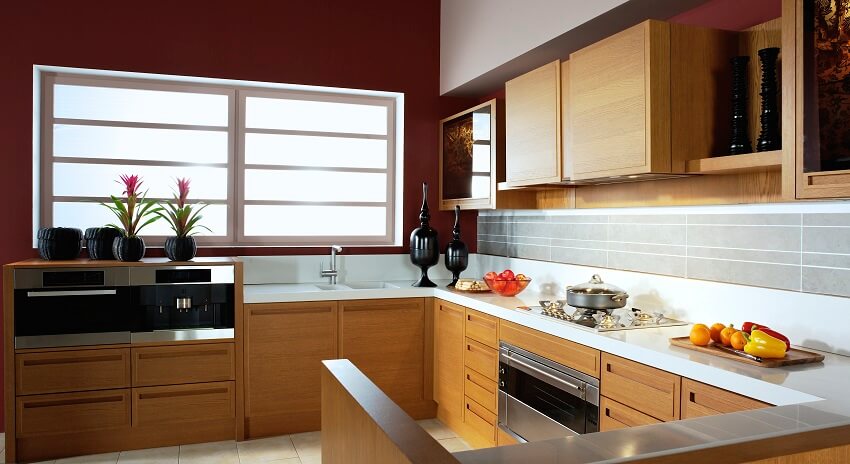 Maroon walls, wooden cabinets, white countertops, and grey backsplash in a modern kitchen